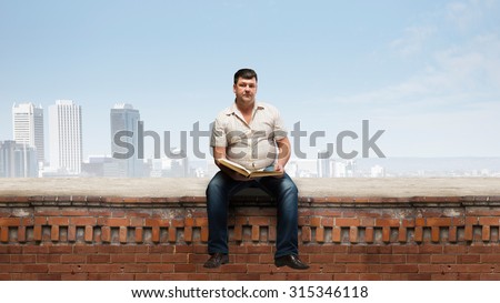 Fat man sitting on building top with book in hands