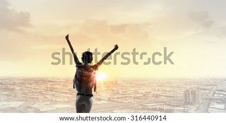 Back view of cheerful woman with hands up facing sunrise