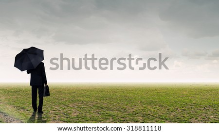 Back view of businessman with suitcase under umbrella