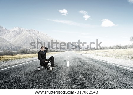 Young funny businessman riding three wheeled bicycle