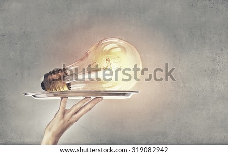 Hand holding tray with glowing light bulb