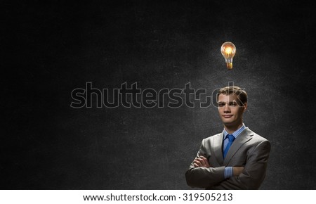 Young confident businessman with arms crossed on chest looking at light bulb
