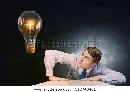 Young man leaning on table and looking at light bulb