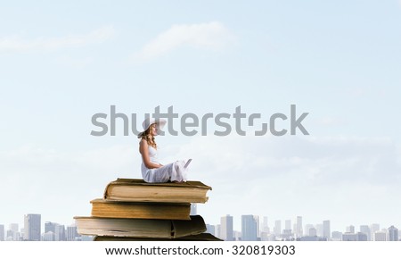 Young lady with laptop on knees sitting on pile of books