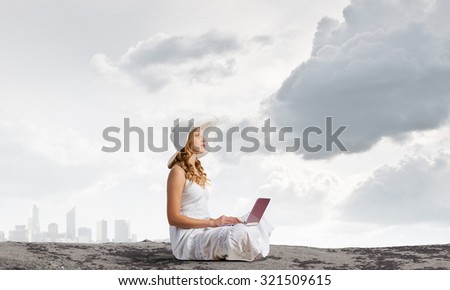 Young lady sitting on top of mountain with laptop