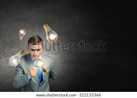 Young businessman looking in magnifying glass at glass light bulb