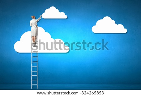 Back view of businesswoman standing on ladder and reaching to cloud
