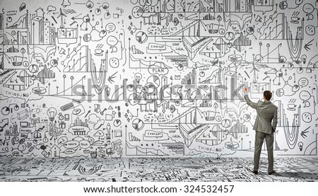 Rear view of businessman drawing business sketch on wall