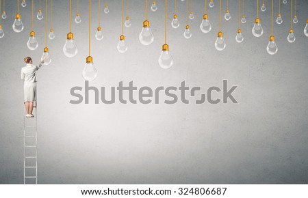 Back view of businesswoman standing on ladder and reaching light bulb