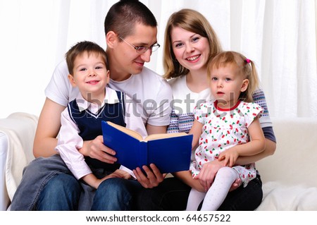 Mom, daughter, son and dad reading a book together on the couch