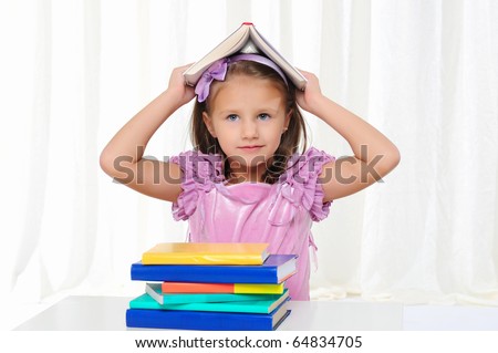 The little girl is studying literature. Reads a book while sitting at a white table.