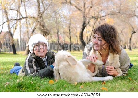 Mother and son together having fun in the autumn park playing with a golden retriever.
