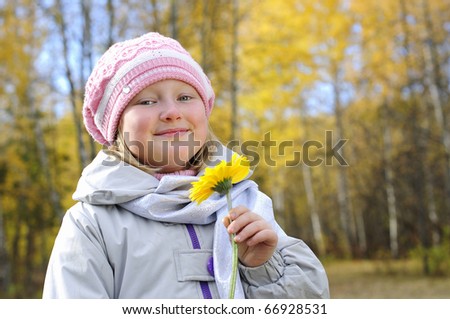 A little girl with a yellow flower in the autumn forest. Portrait.