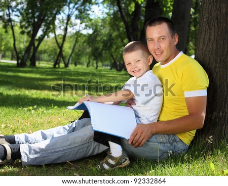 Father with his son reading together in the summer park