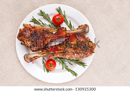 Roasted turkey legs on white plate with cherry tomato and rosemary