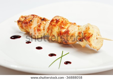 Chicken kebab on skewer in white plate with sauce and onion