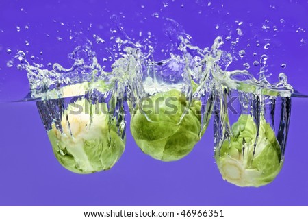 Three Brussels sprouts falling in water on blue with air bubbles