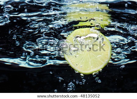 Slice of lime (lemon)  falling in water with air bubbles near surface