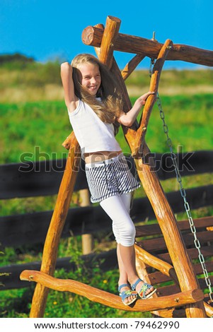 Cute little girl with blond long hair playing on wooden chain swing in rural playground