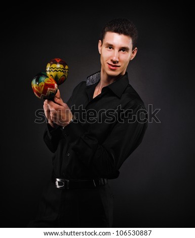 Handsome smiling man with maracas against the black wall