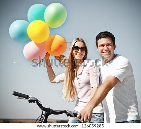 Happy smiling couple with balloons on bicycle in summer day