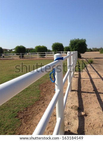 White rail fence on grass bank against blue sky on a horse farm