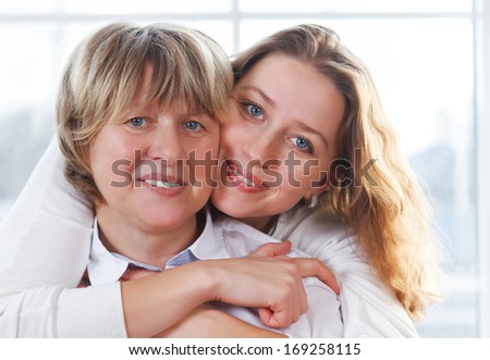 Portrait of a mature mother and adult daughter being close and hugging at home being happy and joyful