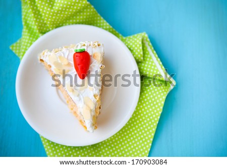 Piece of carrot cake with icing and little carrot on blue wooden background