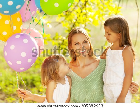 Happy woman and her little daughters in the park with ballons. Mother day or birthday concept
