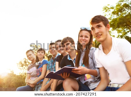 Group of students or teenagers with notebooks outdoors in summer evening