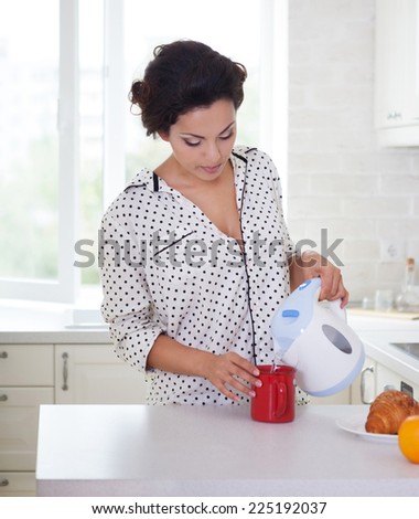 Happy woman preparing a cup of coffee in her kitchen wearing pajamas