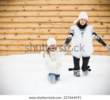 Happy mother with her daughter running outdoors by the wooden house in a winter day