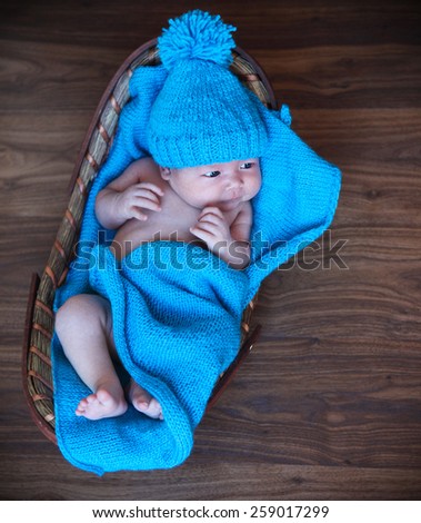 Baby boy laying on blue blanket in the basket on the wooden floor