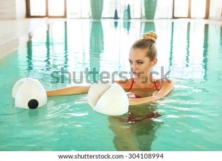 Blond young woman doing aqua aerobics with foam dumbbells in swimming pool at the leisure centre