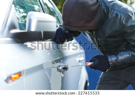 Thief wearing black clothes and leather coat stealing a car