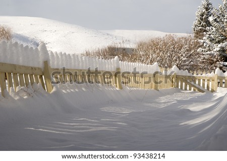 After the storm.  The snow stacks atop a picket fence, creating \