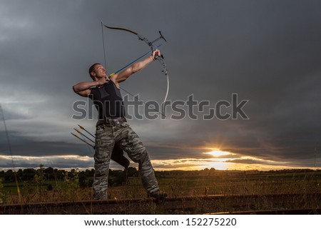 Tough man with bow and arrows during dramatic cloudy sunset.