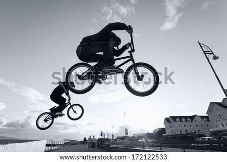 Two Young men performs BMX stunts during sunset at the street. Monochromatic