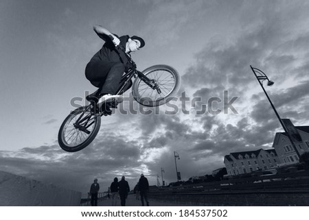 Young man performs BMX stunts during sunset at the street. Blurred motion. Monochromatic