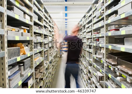 metal shelves with spar parts and technician in motion, person not recognizable