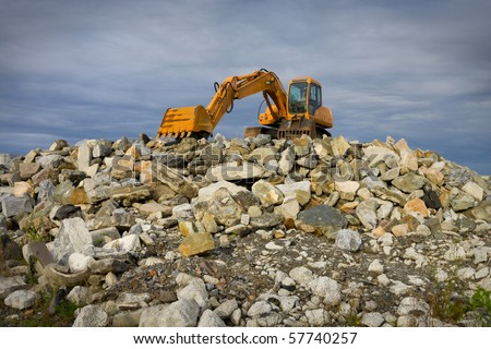 yellow excavator on top of big heap of stones