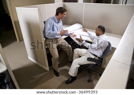 Two male colleagues working in cubicle with blueprints