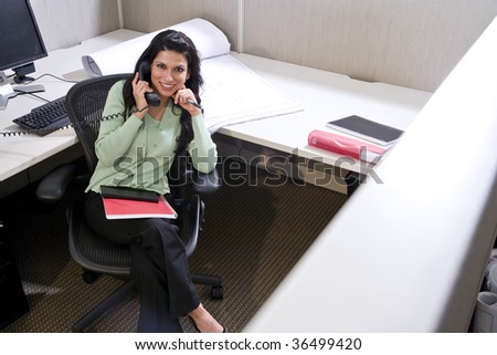 Hispanic woman on phone at office cubicle desk