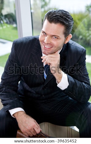 Confident businessman sitting in office by window smiling at camera