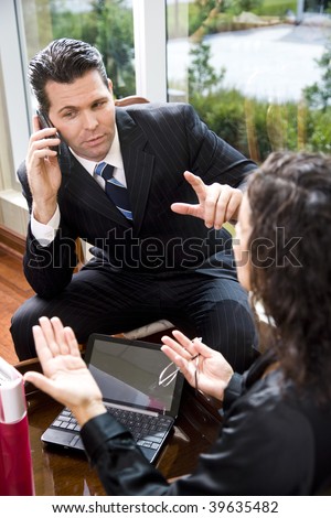 Multitasking businessman in meeting with female Hispanic coworker while listening to mobile phone