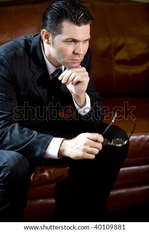 Serious businessman sitting on couch thinking with hand on chin