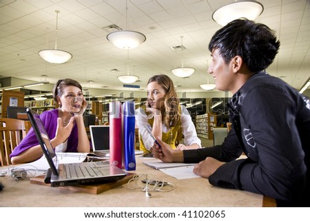 Two pretty female college students studying with handsome male student in school library