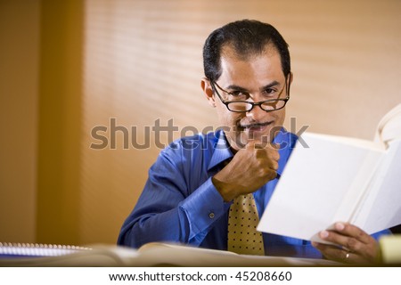 Close-up of serious middle-aged Hispanic businessman working in office reading reference books
