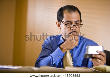 Middle-aged Hispanic businessman working in office holding mobile phone reading text message