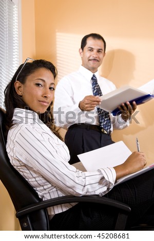 Young African-American office worker with middle-aged Hispanic co-worker in boardroom reviewing report